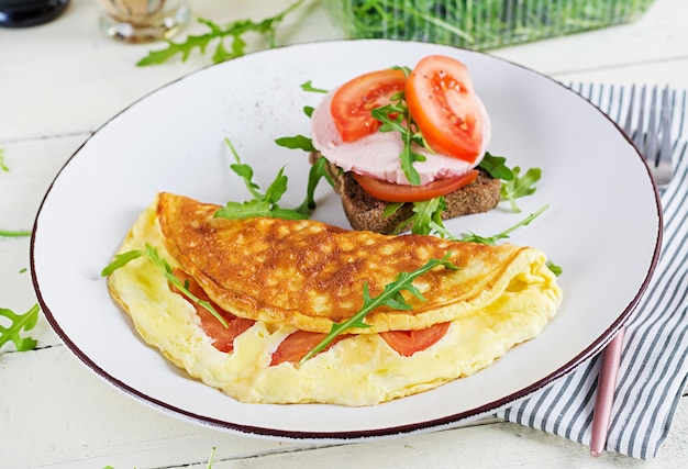 Breakfast. Omelette with tomatoes, cheese and sandwich with boiled sausage.  Frittata - italian omelet.