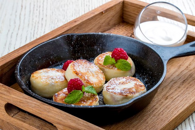 Breakfast in a pan on a white background Cheesecakes with raspberries and sour cream On a wooden tray