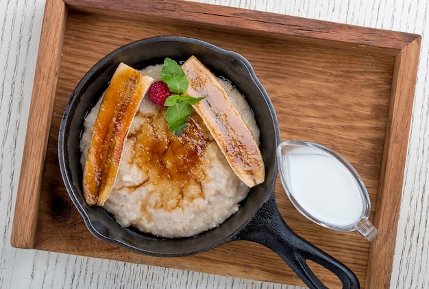 Breakfast in a pan on a white background Oatmeal with banana and syrup On a wooden tray