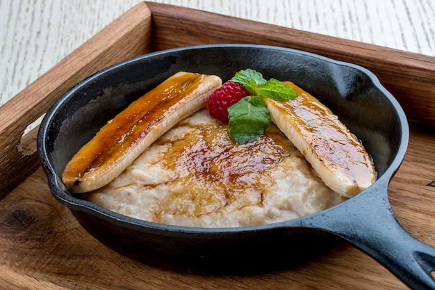 Breakfast in a pan on a white background Oatmeal with banana and syrup On a wooden tray