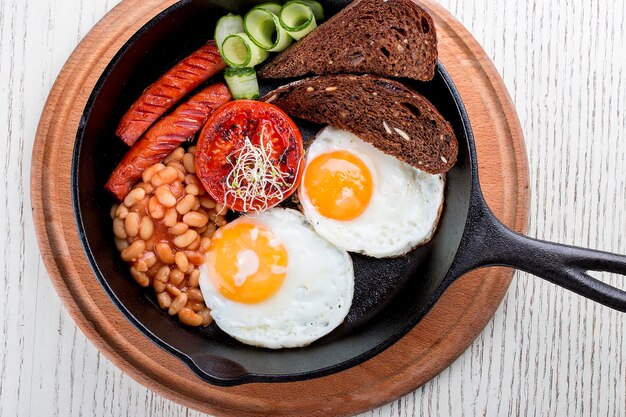 Breakfast in a pan on a white background Scrambled eggs with beans toast and sausages