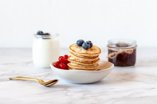 Breakfast of pancakes decorated with blueberries and redcurrants, yoghurt and jam, selective focus