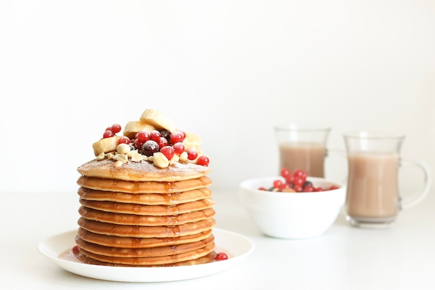 Breakfast pancakes with berries are stacked, berries and cocoa in the background.