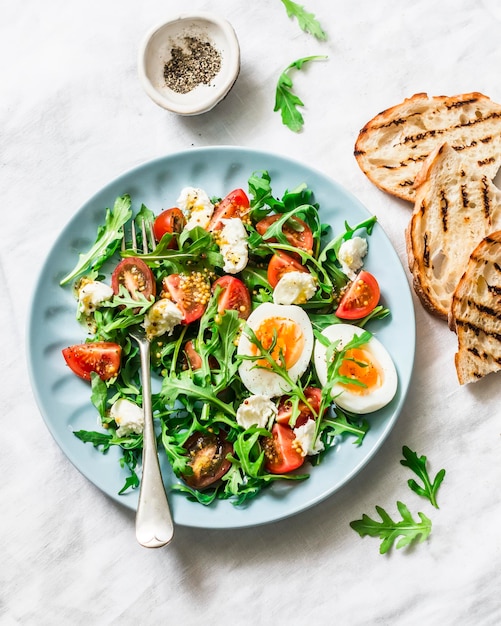 Breakfast salad arugula cherry tomatoes mozzarella and boiled egg with olive oil mustard lemon dressing on a light background