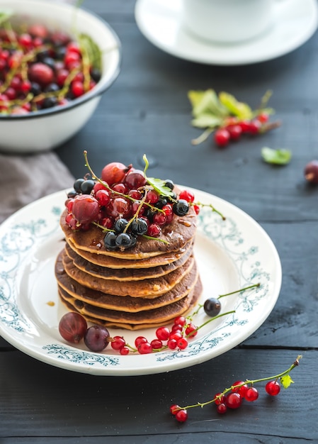 Breakfast set. Buckwheat pancakes with fresh berries and honey on rustic plate over black wooden table.