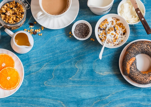 Breakfast setting over blue table with copy space border Yogurt pumpkin granola bagel butter Top view