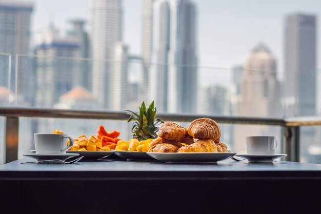 Breakfast table with coffee fruit and bread croisant on a balcony against the backdrop of the big city