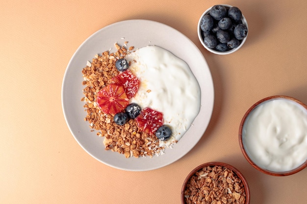 Breakfast table with granola bowl with greek yogurt decorated by blood oranges blueberry and coconut beige background ingredient for breakfast top view