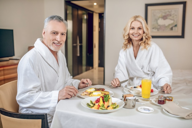 Breakfast time. A couple in white robes having breakfast and looking pleased