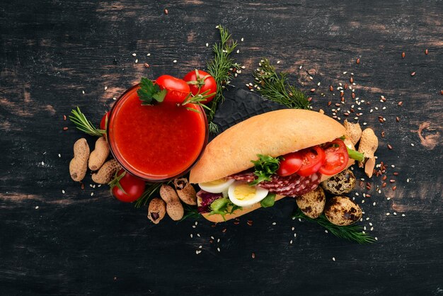 Breakfast Tomato juice and burger with salami and vegetables On a wooden background Top view Copy space