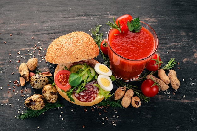 Breakfast Tomato juice and burger with salami and vegetables On a wooden background Top view Copy space