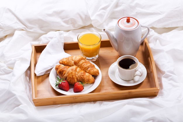 Breakfast tray in bed coffee croissants juice and fresh strawberries