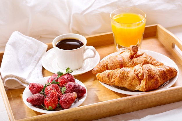 Breakfast tray in bed : coffee, croissants, juice and fresh strawberries