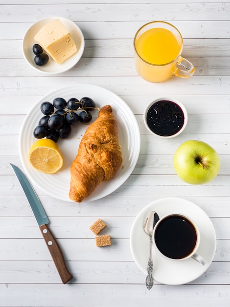 Breakfast on a White Table Coffee Croissant Orange juice Grapes Apple Chocolate.