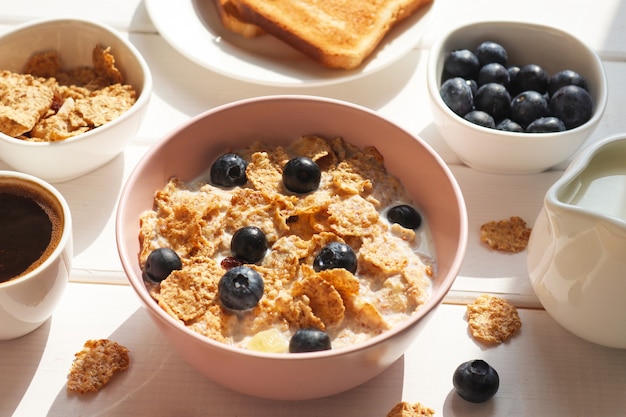 Breakfast of whole wheat flakes with milk blueberries coffee and toast closeup on wooden table