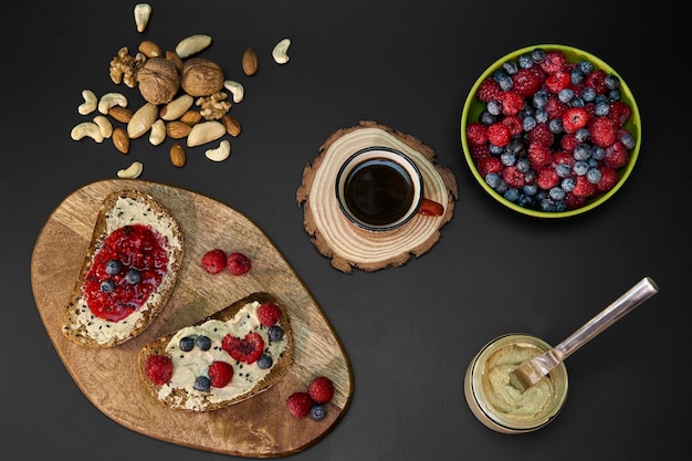 breakfast with coffee cup and toasted bread berries cashew butter and nuts on black background