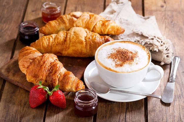 Breakfast with cup of cappuccino coffee with croissants on wooden table