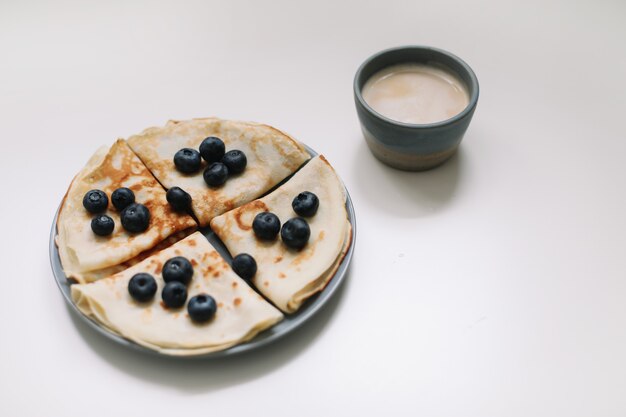 Breakfast with a cup of cappuccino and pancakes with blueberries on a white background top view