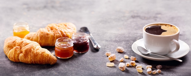 Breakfast with cup of coffee, croissant and fruit jam on dark table