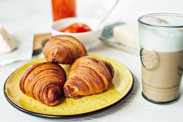 Breakfast with a fresh croissant and a cup of aromatic coffee latte, tangerine jam, butter and brie cheese. Healthy breakfast.