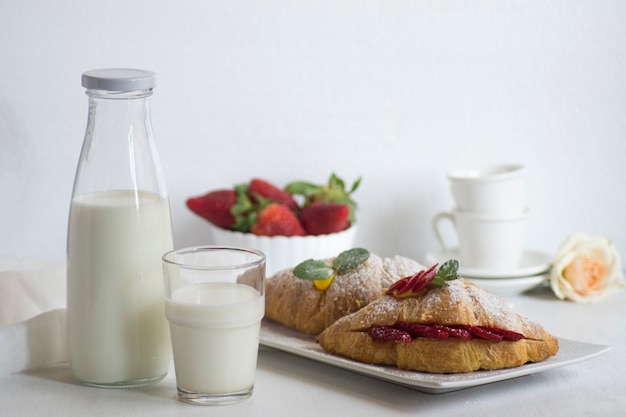 Breakfast with fresh milk, croissant and strawberries on white surface