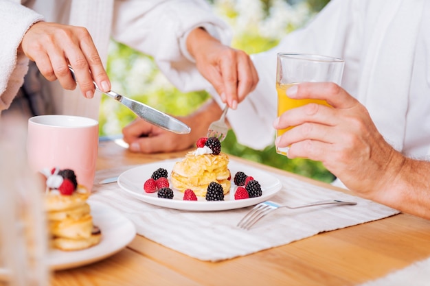 Breakfast with pancakes. Mature man having nice warm pancakes with honey and berries for breakfast and glass of orange juice