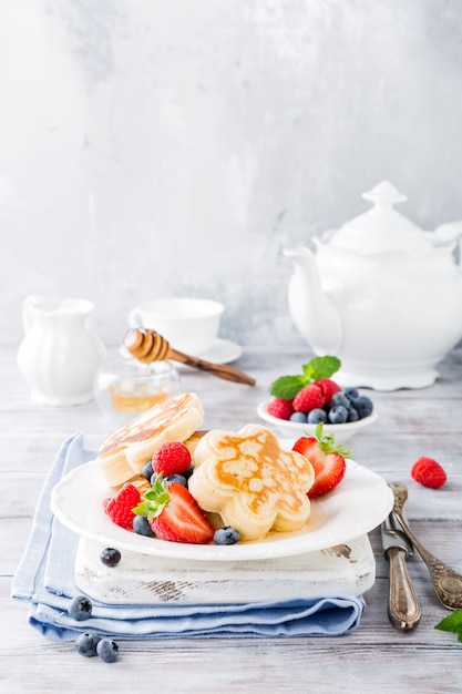 Breakfast with scotch pancakes in flower form, berries and honey on light wooden table. 