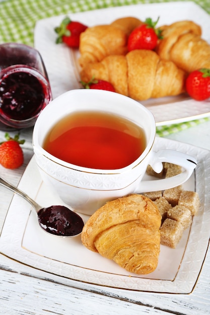 Breakfast with tea, jam and fresh croissants on wooden