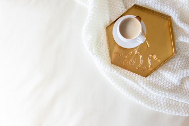 Breakfast for the woman in bed. Coffee in a white mug. Nordic style. White knitted plaid. Bouquet of flowers.