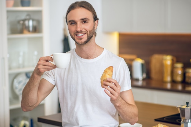 Breakfast. Young man in homewear standing in the kitchen with a coffee cup in hand