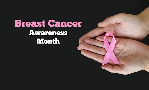 Breast Cancer Awareness Month Woman hands holding pink ribbon on black background