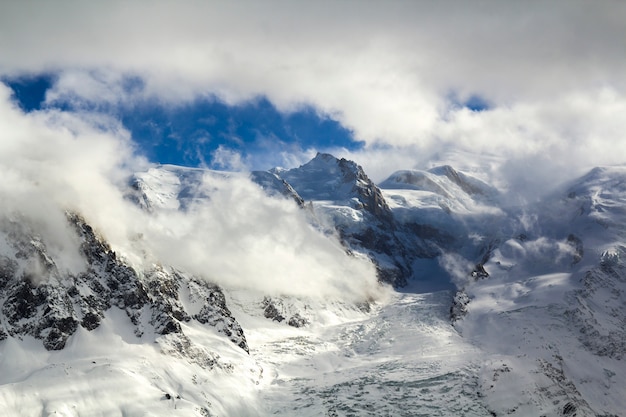 Breathtaking aerial view of Mont Blanc mountain peak covered with shiny snow, ice and glaciers under blue sky with puffy white clouds on the French side of Alps on a clear cold sunny winter day