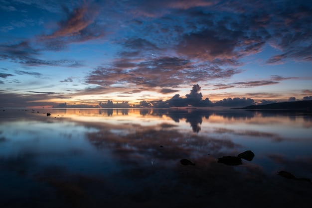 Breathtaking sunrise on the beach, colorful clouds reflecting in the smooth sea like a mirror.