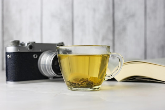 Photo brewed herbal green tea in a transparent cup next to an open book and a vintage camera