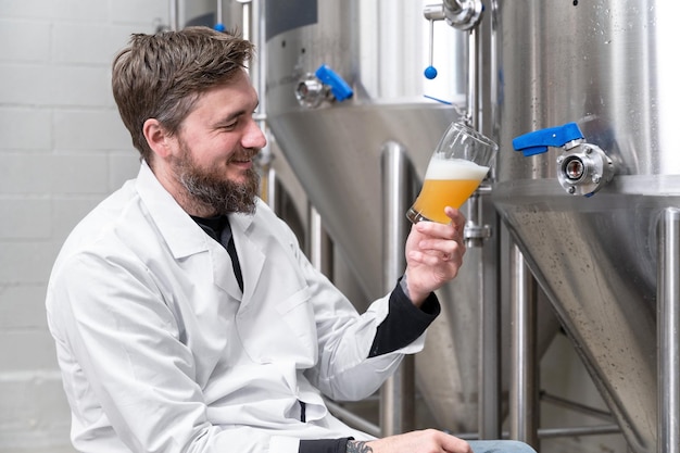 Brewer wearing white coat controlling process of beer fermentation while working at modern beer factory