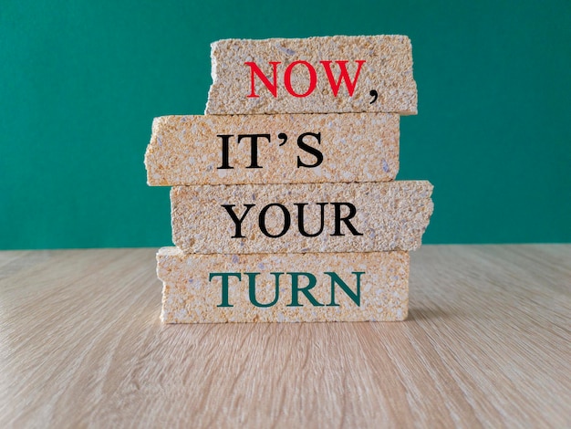 Brick blocks form the words 039now it039s your turn039 on a wooden table Beautiful green background