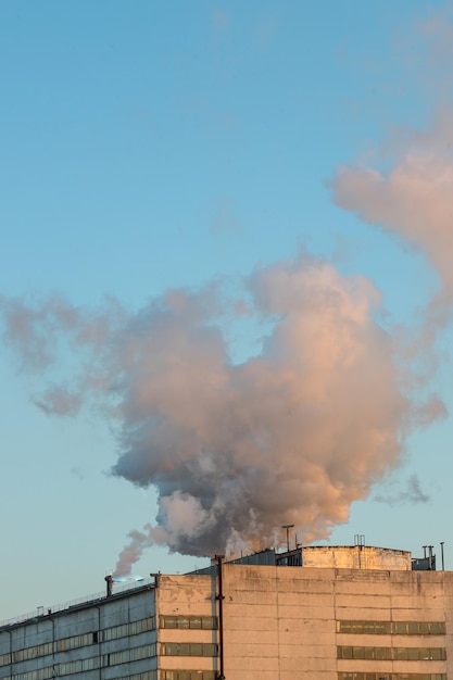 Brick chimney with white smoke over an industrial building