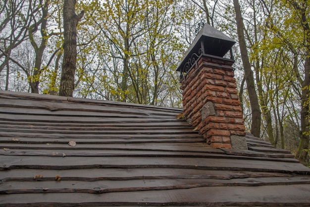 Brick chimney with wrought iron peak above iron curlicues on a wooden plank roof on rainy day