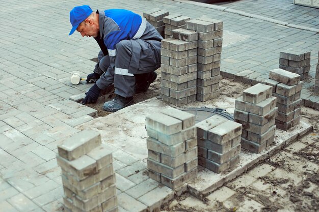 Bricklayer lays paving slabs outside Working man performs landscaping Builder lays out sidewalk with stone blocks