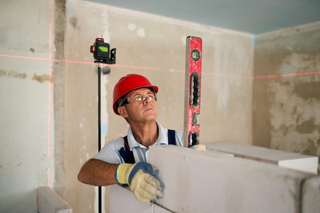 Bricklayer using spirit bubble and laser level to precise check concrete blocks on wall contractor