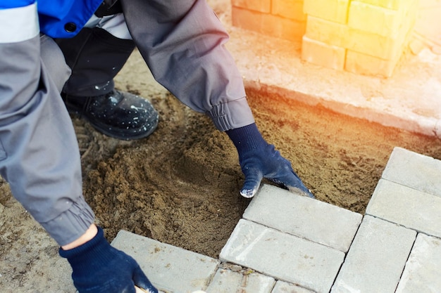 Bricklayer in work clothes sits on sidewalk and lays out paving slabs Sight of working man in open air