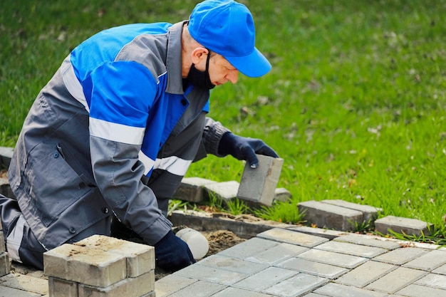 Bricklayer in work clothes sits on sidewalk and lays out paving slabs Sight of working man in open air