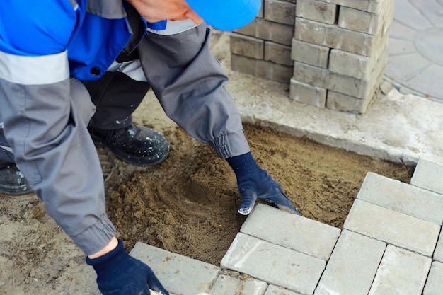 Bricklayer in work clothes sits on sidewalk and lays out paving slabs Sight of working man in open air