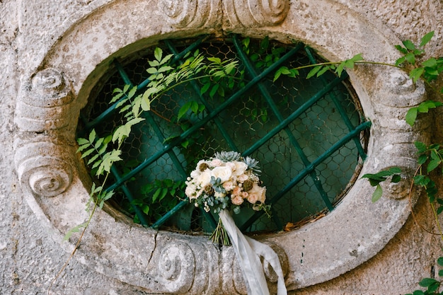 Bridal bouquet on an oval window of an ancient house