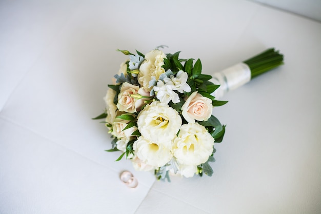 Bridal bouquet and rings lie on white sofa