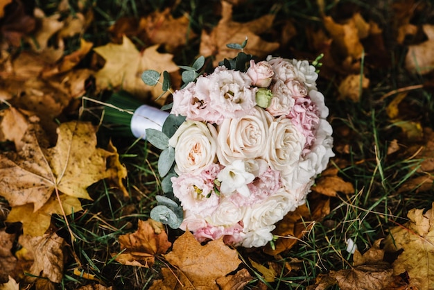 Bridal bouquet with gentle pastel flowers and pink roses and greenery lying on the grass Autumn bridal bouquet on yellow and orange fall leaves Composition design gold autumn flat lay top view