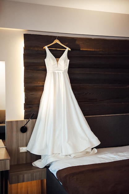 Bridal wedding dress hanging on hanger in the room in early morning