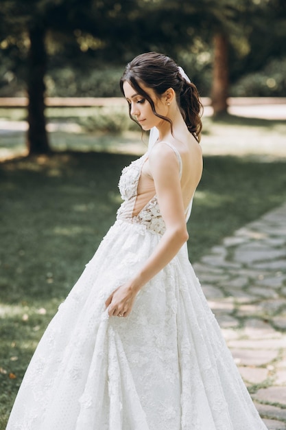 the bride in a beautiful white dress stands in the middle of a green forest