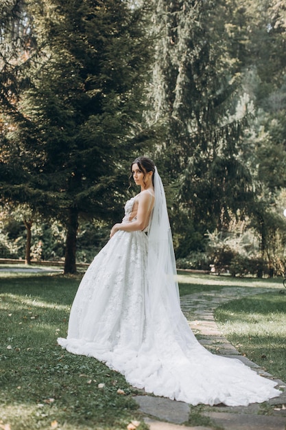 the bride in a beautiful white dress stands in the middle of a green forest