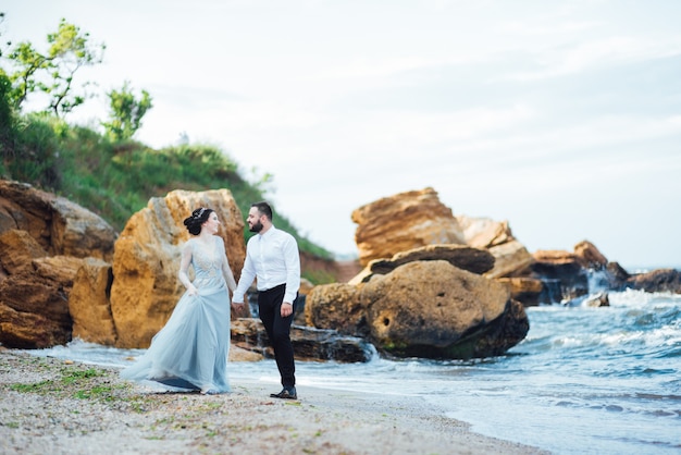 bride in a blue dress walk along the ocean shore